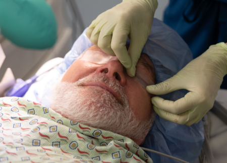 CRNA prepping an older adult for anesthesia by placing tape on eyes