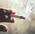 A hand holding a cigarette with smoke.