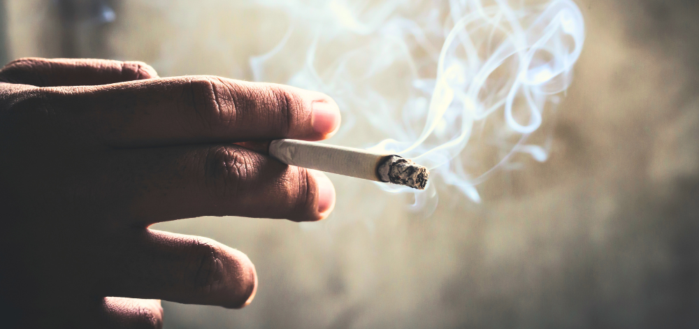 A hand holding a cigarette with smoke.