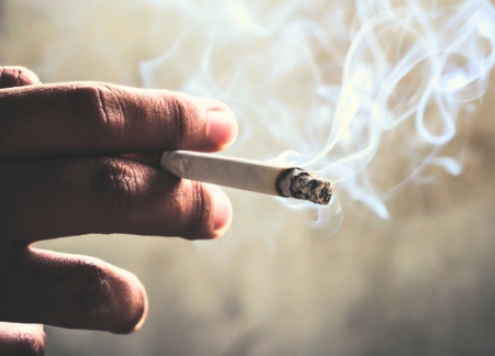 A hand holding a cigarette with smoke.