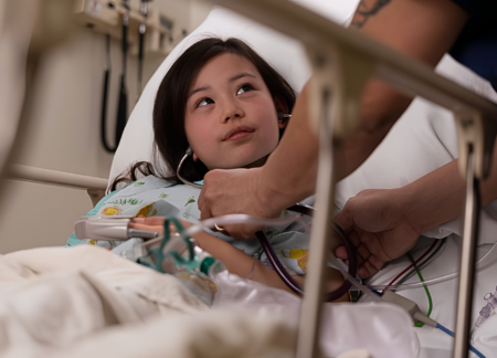 A young child in bed looks up at a CRNA